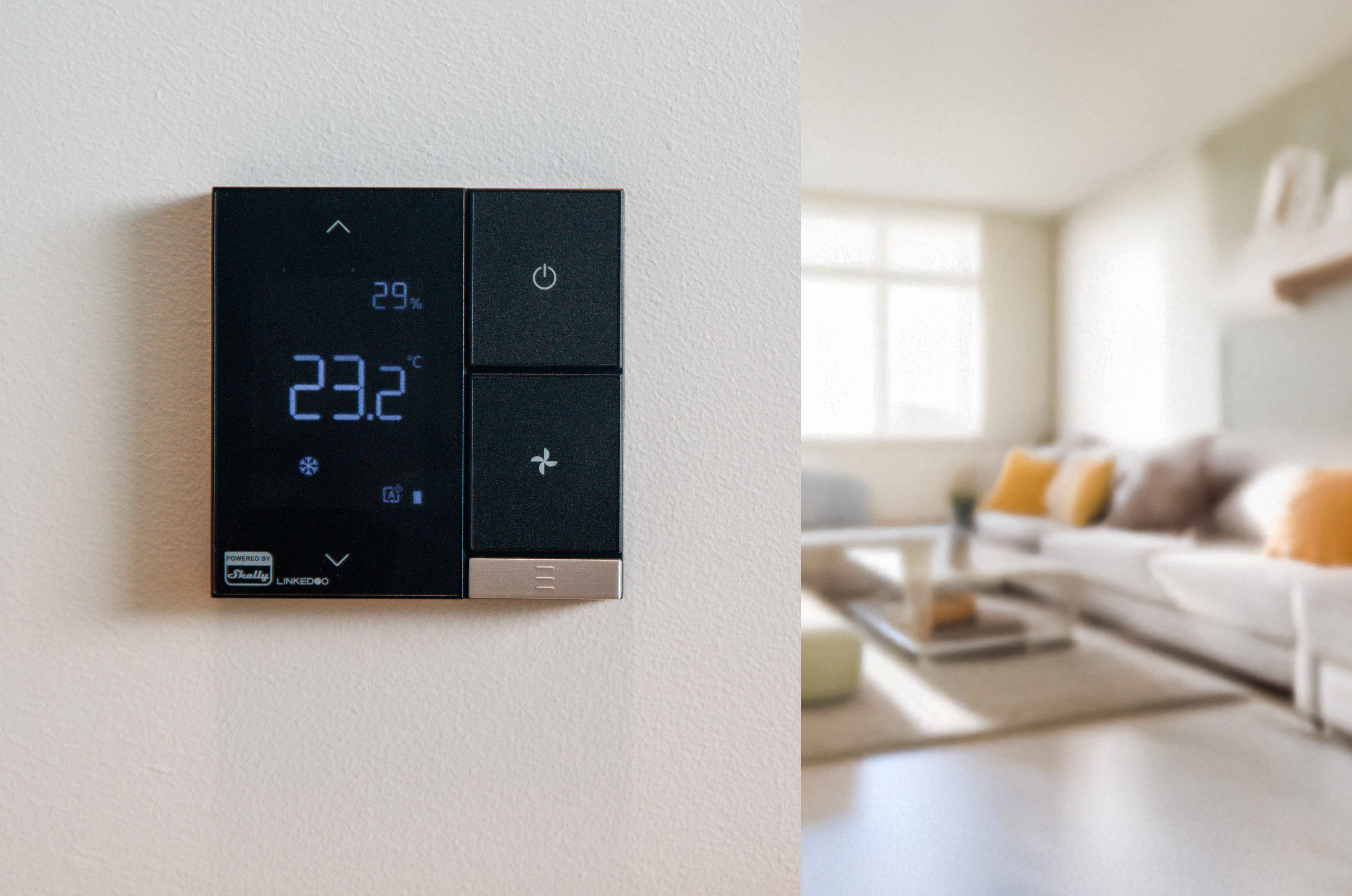 LinkedGo ST802-B smart thermostat installed on a wall in a modern living room, with the screen displaying temperature and system settings during normal operation.